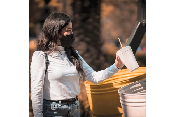 A girl throwing away a single-use cup in the trash.